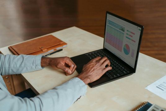 Hände von einem Mann die an einem Laptop arbeiten.