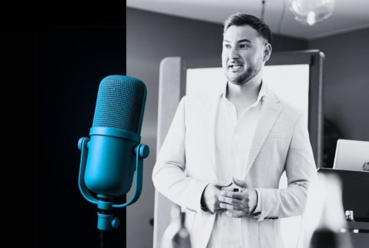 Philipp Kaufmann steht lächelnd in einem hellen Raum, im Vordergrund ein grosses Mikrofon.