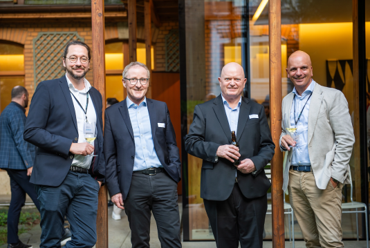 Vier Männer stehen vor einem Holzgebäude