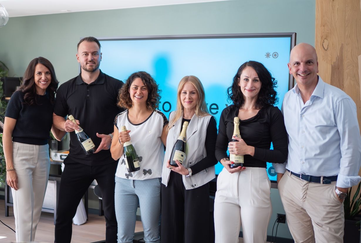 6 people standing next to each other holding each a bottle of champagne